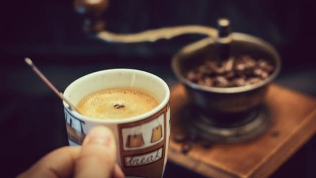 Kahvikuppi ja käsikäyttöinen kahvimylly kahvipapuineen